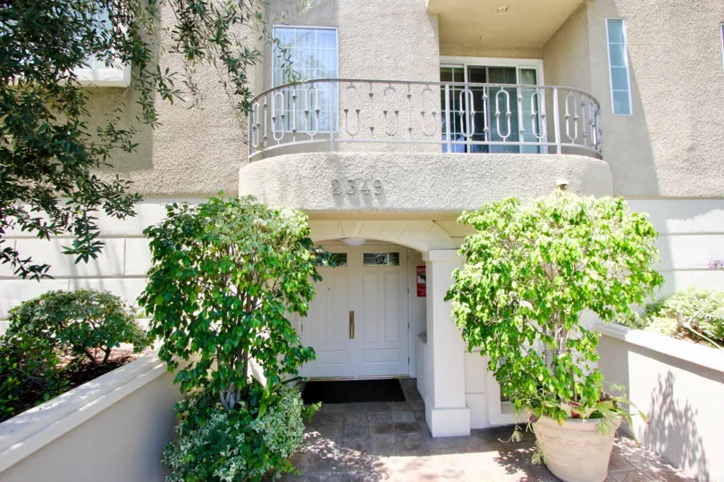A balcony sits over the entrance to 2349 Beverly Glen. Two potted saplings sit on either side of the entrance.