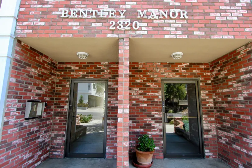 THE PLACE LOOKS LIKE A OFFICE WITH TWO GLASS DOORS AND A SMALL TREE PLANT NEAR THE ENTRANCE