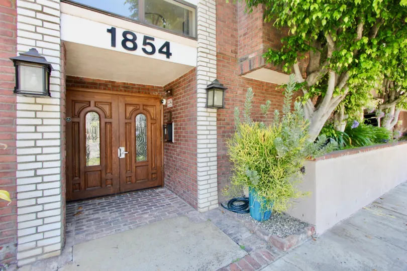A red brick house in the Beverly Glen Villas neighborhood with a wooden front door and green trees