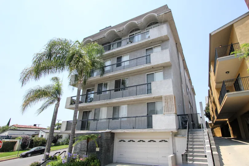 A side view of The Holmbly View, a residential building with palm trees and a garage.