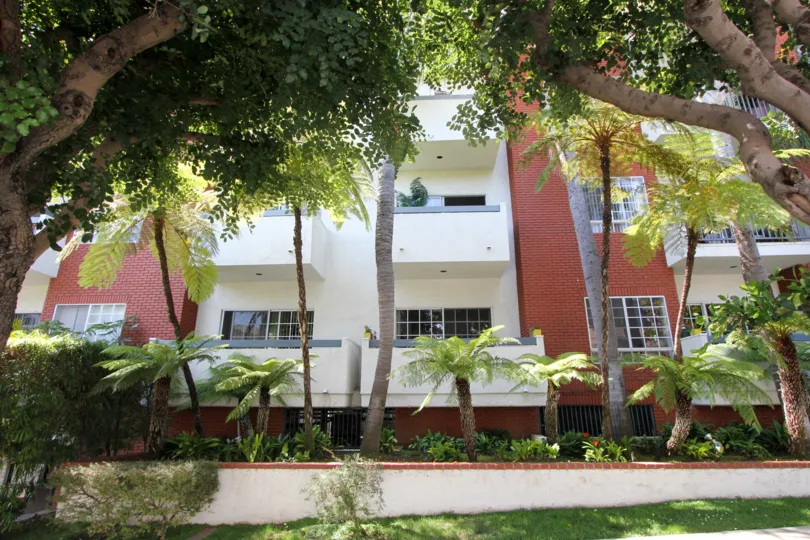 Exterior view of balconies at Kinnard Village in Westwood, California on a sunny day with a canopy of trees in front.