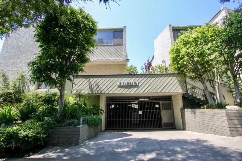 A view of apartment windows, trees and plants surrounding the security door of a parking garage at Thayer Townhomes