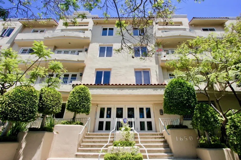 Exterior view of front entrance, stairwell, and balconies of The Beverly Westwood in Westwood, California on a sunny day