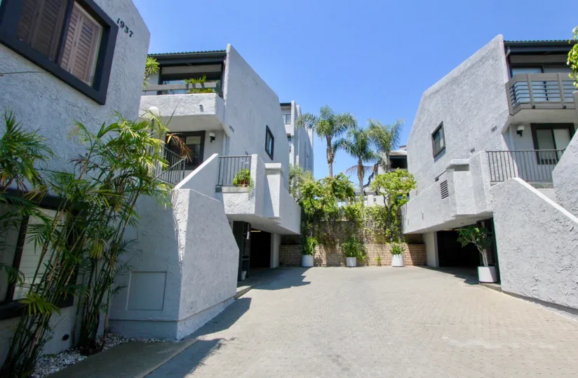 Two grey buildings in the Villa Glen Townhomes neighborhood with black windows and palm trees