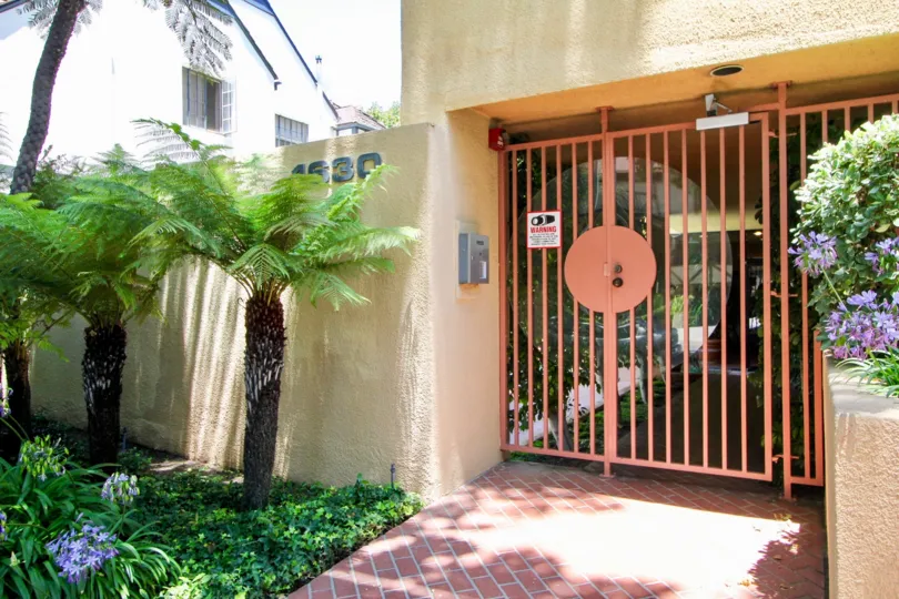 A yellow house at the Walden Condos neighborhood with a red gated fence and small palm trees