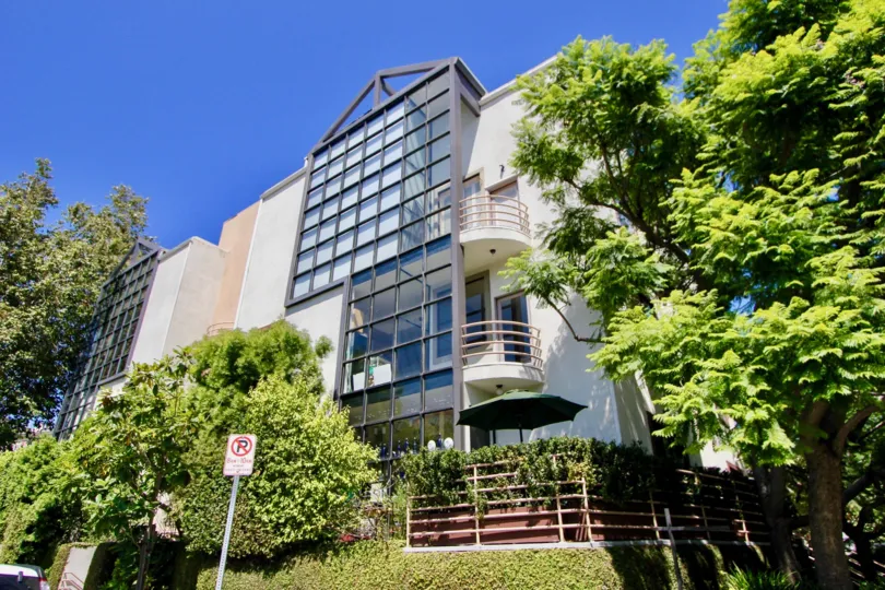 A brightly lit glass facade and balconies over verdant trees at West Breeze.