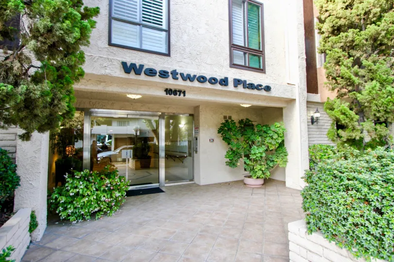 The Westwood Place, with multiple green plants and shrubs in front of it and a large glass door