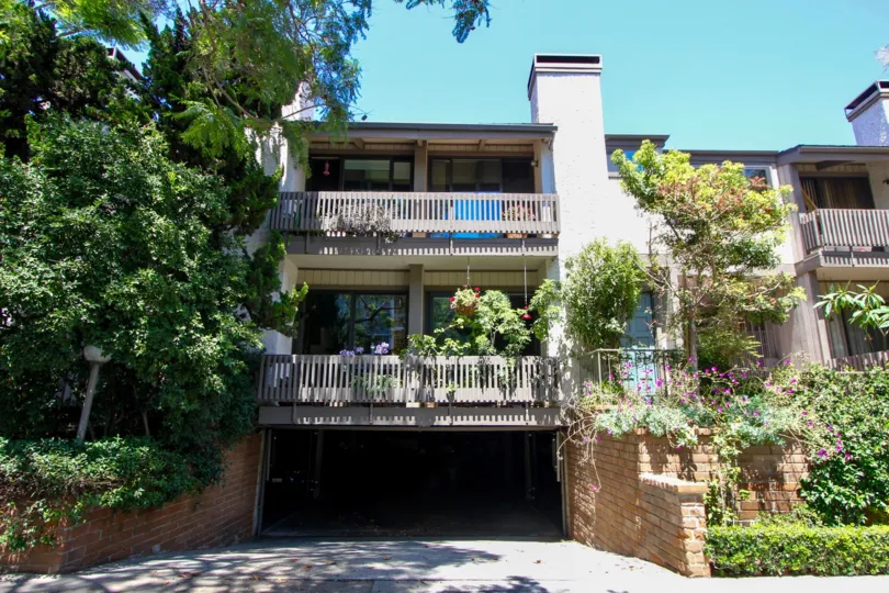 A tan house in the Woodvale Village neighborhood with two balconies and many trees and plants