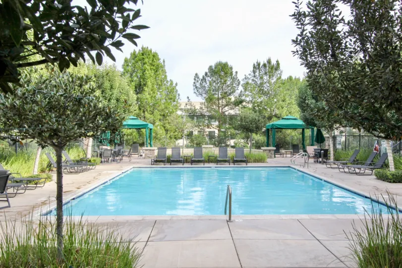 Nice sized outdoor swimming pool featuring several lounge chairs and sun shield canopies.