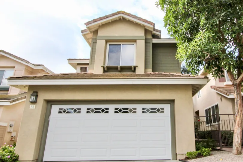 2 storey home with double car attached garage, stucco siding and mature tree with decorative car door at the Cottages