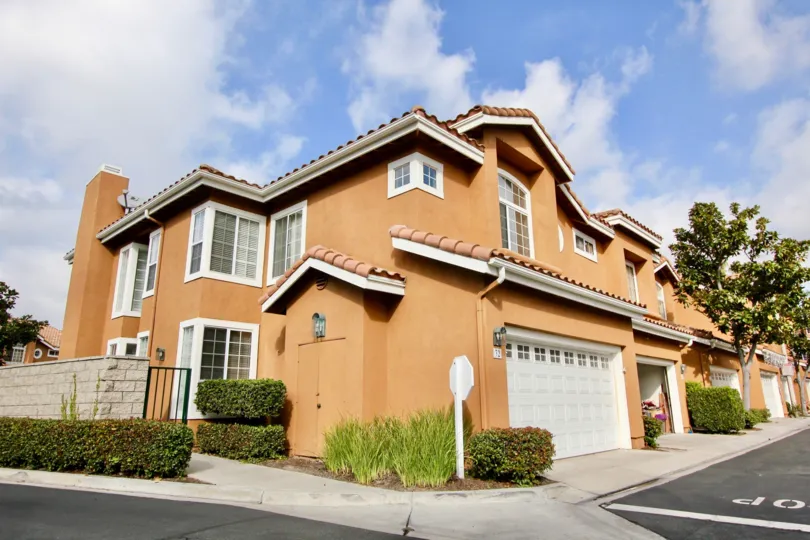 Corner unit home with double car garage, adjacent sidewalk and petite hedges with spanish inspired roof in Aliso Viejo