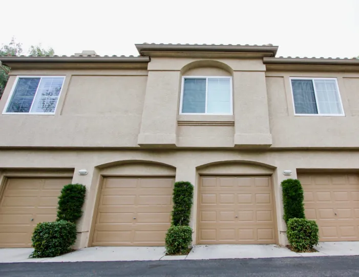 A building featuring three upstairs windows and four garages, adorned with topiary, in Seacove Place.