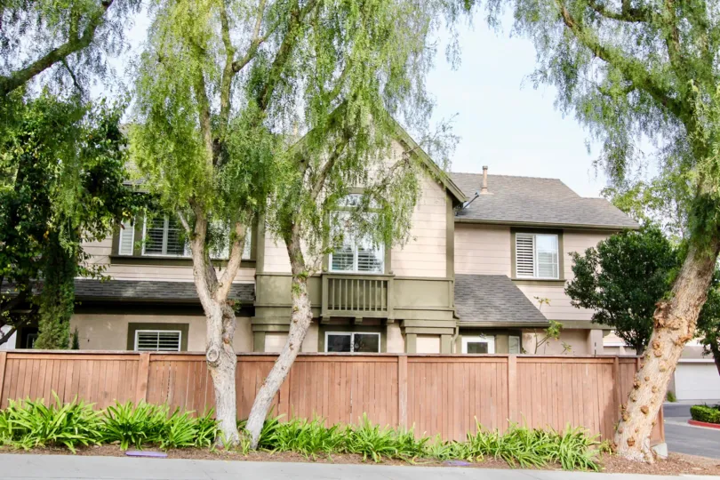 A light wood fence and tall trees surrounds a two story Twelve Picket Lane home.
