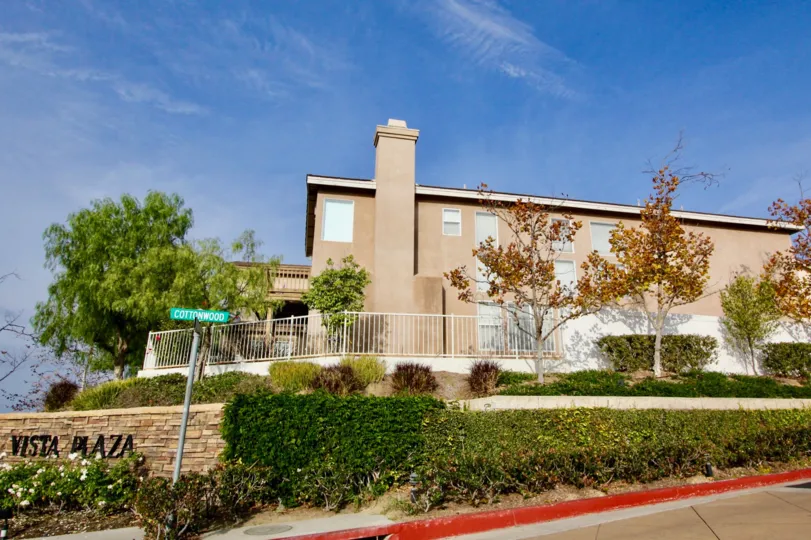 Sunny sky with a building and fence and bushes and trees in the Vista Heights Community in Aliso Viejo, CA.