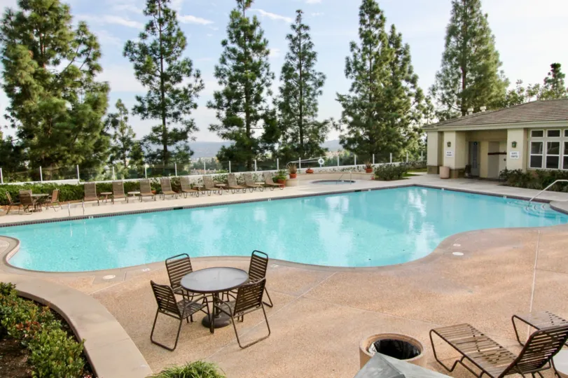 Community swimming pool with large pool deck, tall trees for privacy and adjacent pool house in Vistas Above Wood Canyon