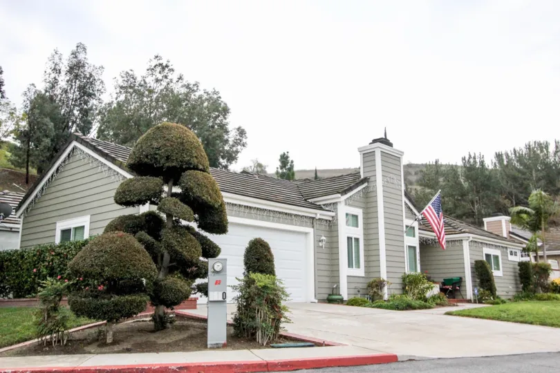 a house with grey colour and a flag on the front and greenery around