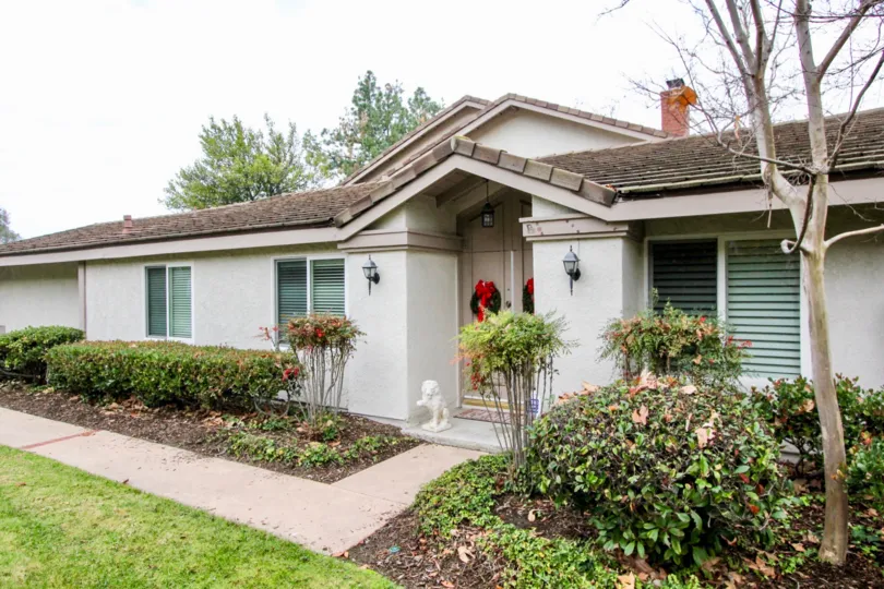 entrance front view of a white one floor house with bushes and greenery around