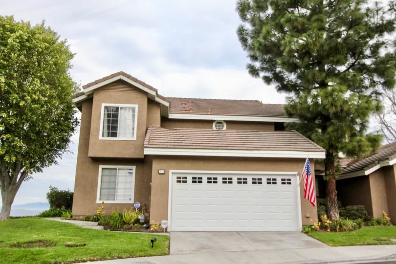 Street view of two-story home with lawn and trees, tan stucco with white trim, in Horizons, Anaheim Hills, CA