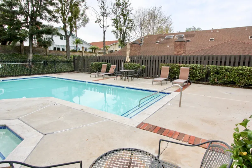 pool with an L shape with house in background and chairs and bushes around