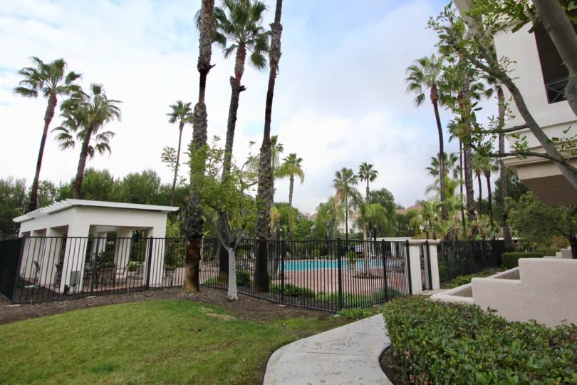 A cloudy day in Viewpointe with a swimming pool behind a gate, surrounded by palm trees.
