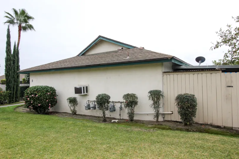 Side of a white home with grass and bushes on a cloudy day