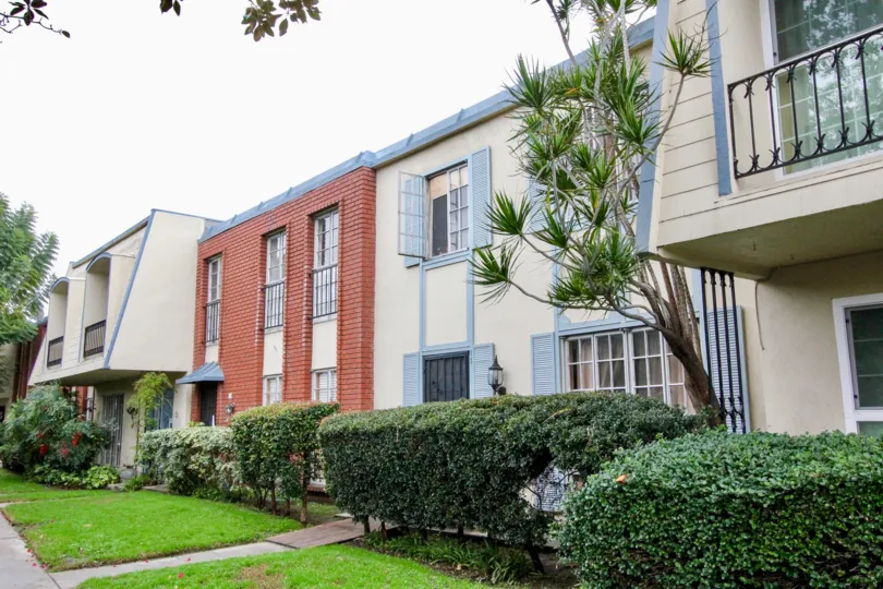 A complex at Anaheim Village III with a partially bricked front, blue shutters, and mature hedges