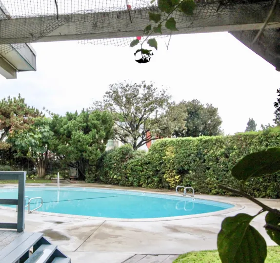 Inviting oval shaped swimming pool in Anaheim Village III, Anaheim, California, is surrounded by trees and a hedge for privacy.