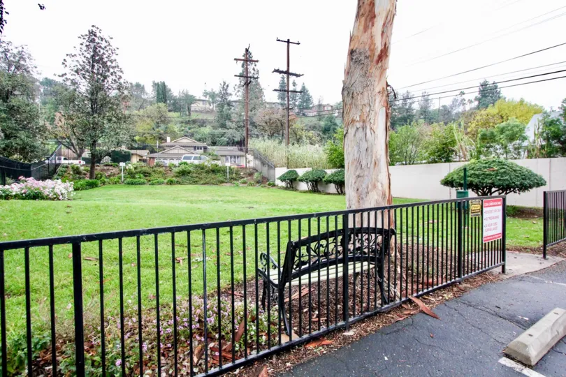 A wide black iron gate with a bench and tree inside Casa Canon in Anaheim CA