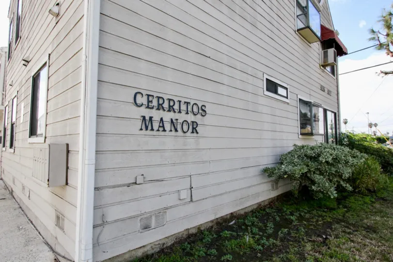 Side of a white paneled building with bushes on the side
