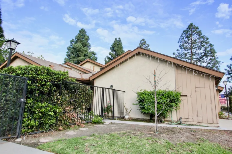 a warm day in the Laurelwood Village with a house gate closed and around the trees and roofless top and one flag in side