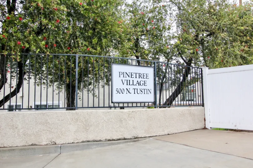Trees hanging over a sign advertising Pinetree Village Village in Anaheim, CA