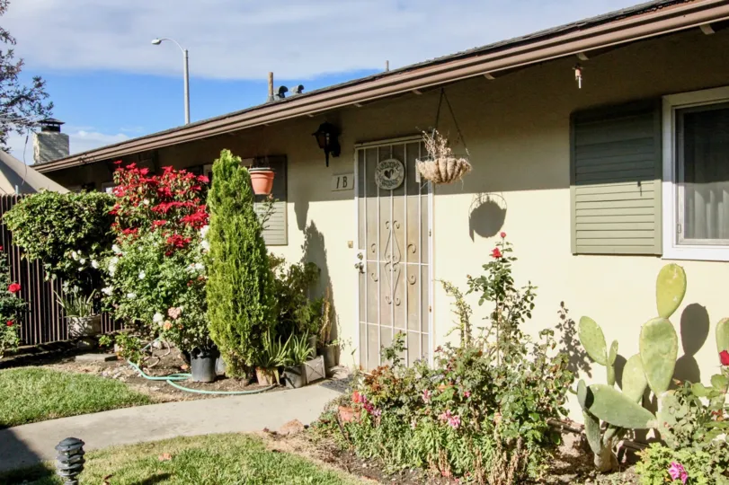 THE FRONT OF THE HOUSE WITH MANY PLANTS WITH FLOWERS, LAWN, NUMBER ON THE WALL ARE SHOWN IN ANAHEIM CITY