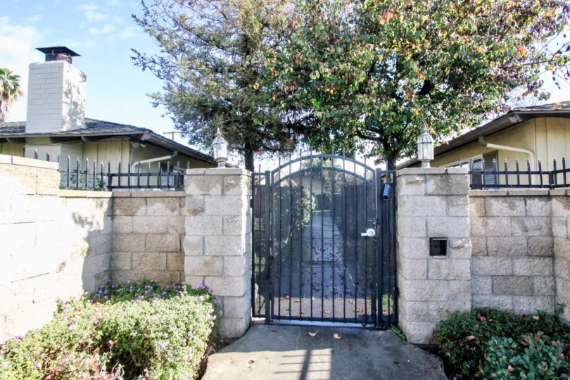 A black gate in The Pines with two treesand house.