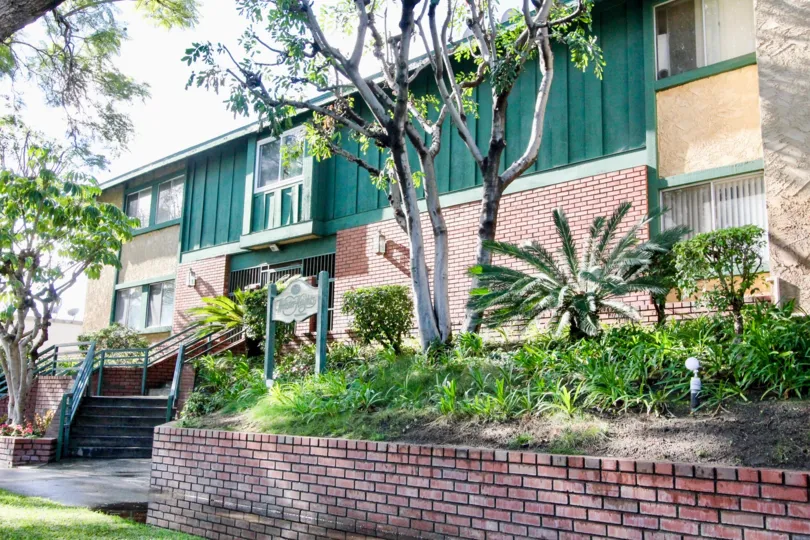 THIS IMAGE REPRESENTS THE FRONT OF THE HOUSE IN ANAHEIM THAT SHOWS MANY PLANTS, TREES PATHWAY