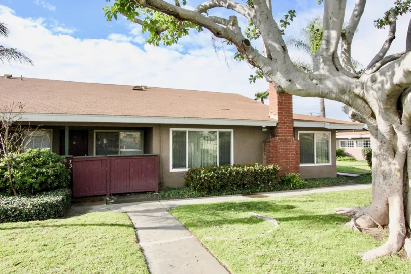 a warm day in the wilshire westmont with a house that has entrance gate closed and toll tree in right side on garden around