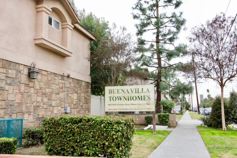 THIS IMAGE SHOWS THE SIDE VIEW OF THE HOME WHICH IS IN BUENA PARK, THAT HAVE NAME BOARD, PATHWAY, PLANTS AND TREES