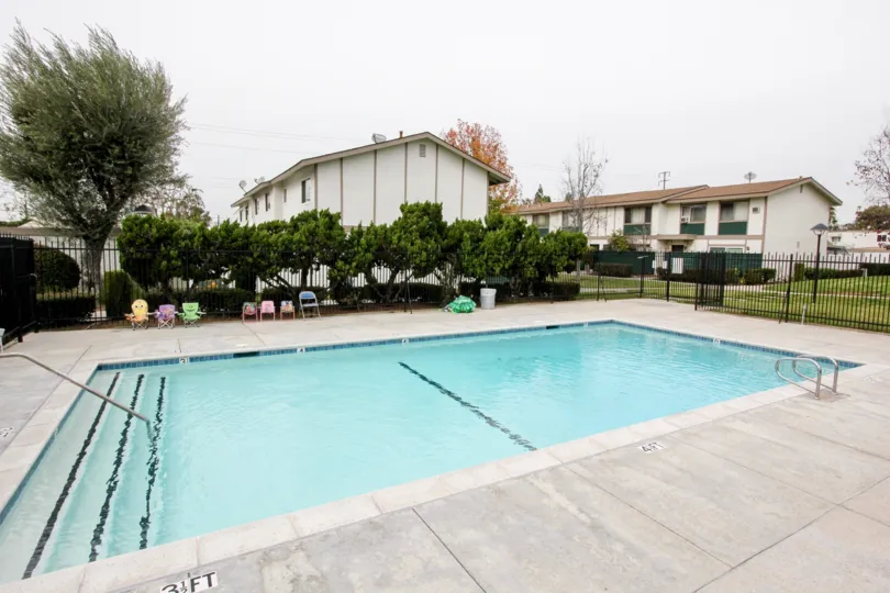 a rainy day in the highland greens with a building that has swiming pool water clearness and 7 chairs in front and trees around