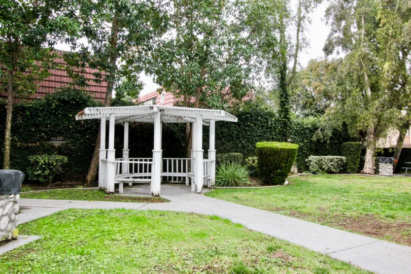 THIS IMAGE SHOWS THE GARDEN WITH RESTING PLACE ON THE PATHWAY, LAWN, LOT OF TREES, PLANTS LOCATED IN BUENA PARK