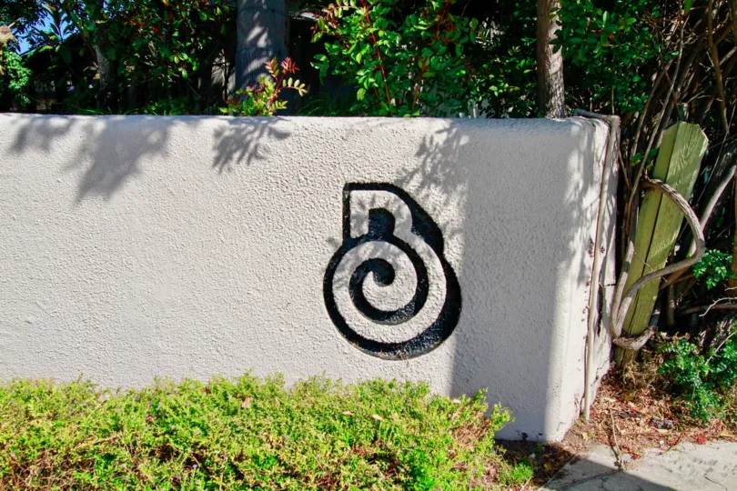Grey cement barricade, with interesting black design, separating vegetation and wooden structure