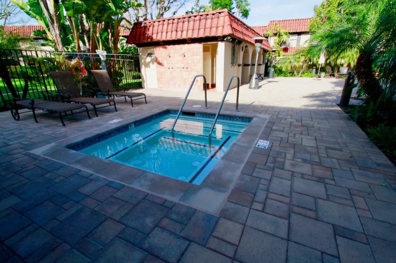 A SMALL SWIMMING POOL WITH THREE SITTING PLACES AND TWO TO THREE HOUSES ARE LOCATED AT THE BACK SIDE OF THE POOL AND SOME TREES ALSO NEAR TO THE POOL. IT LOOKS LIKE A KID POOL.