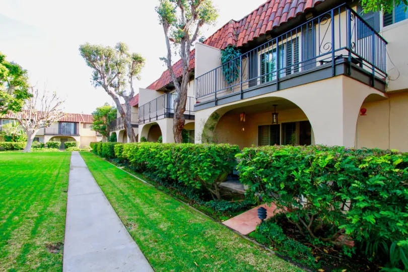 Country Club Villas sidewalk with bushes and trees on a sunny day.