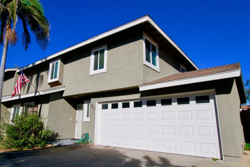 A gray home, on a sunny day with a palm try in the yard. This home in Costa Mesa also has lots of green plants.