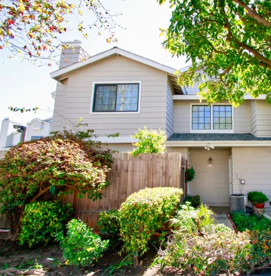 rear view of a two level residence featuring fence and greenery