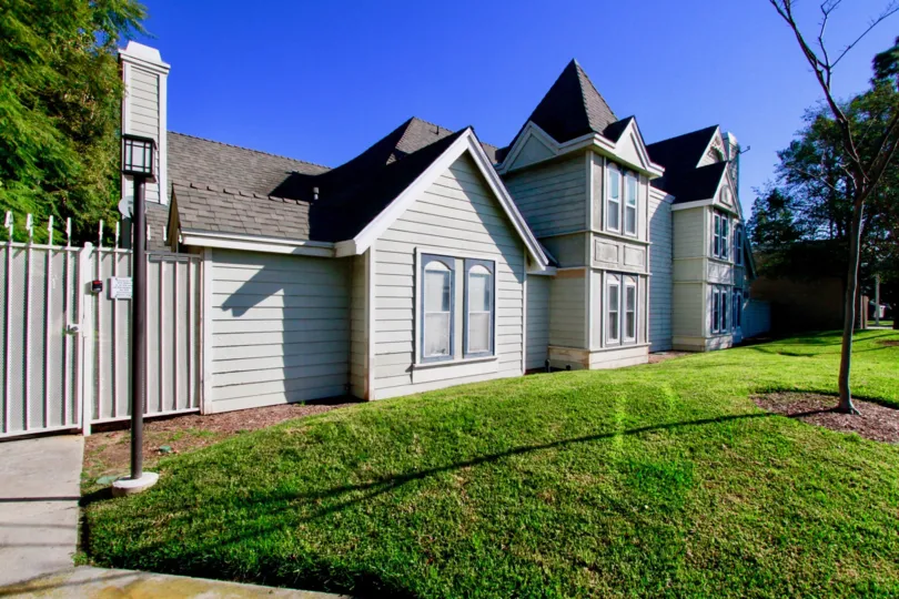 A gated grouping of small homes, that seems to have a large front yard with a tree, and light.