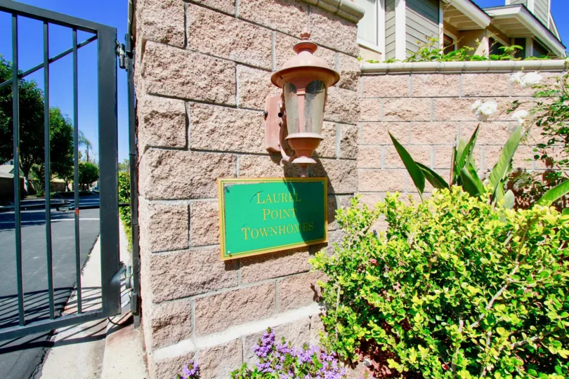 A green Laurel Point entrance sign below a pink light, next to an iron gate.