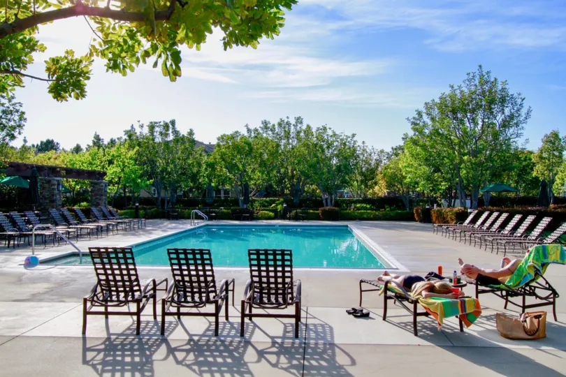 THE SWIMMING POOL LOCATED IN THE OUTSIDE AND SOME SITTING CHAIRS ALSO AVAILABLE FOR RELAXATION AND THE SUN ALSO HOT SOME TREES ALSO NEAR TO THE POOL