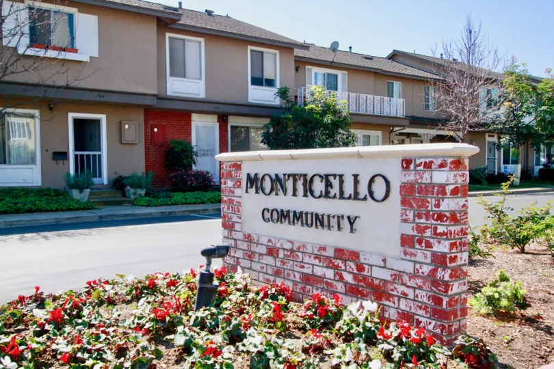 THE APARTMETS WITH THE FRONT SIGN BOARD WITH RED COLOUR BACKGROUND THAT REPRESENTS MONTICELLO AND THE BALCONY OF THE FIRST ONE IS OPENED AND SOME PLANTS NEAR TO THE SIGN