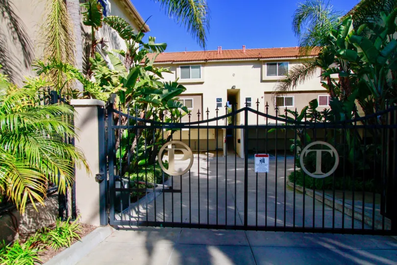 A big house with a big gate in the Palermo Townhomes with palm trees and flowring plants near the road