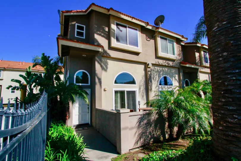 A home in the Palermo Townhomes with a fence and palm trees on a sunny day.