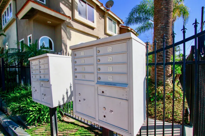 Palermo Townhomes mailboxes next to a fence and palm trees on a sunny day.